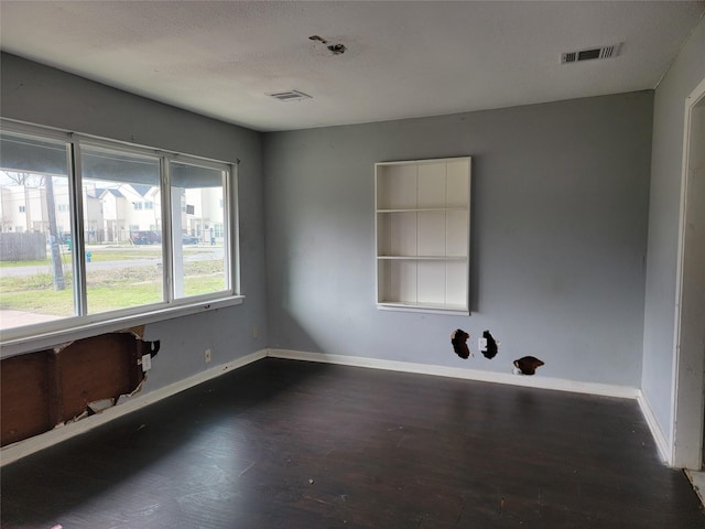 empty room with visible vents, a textured ceiling, baseboards, and wood finished floors