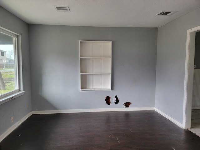 empty room featuring baseboards, visible vents, and dark wood-style flooring