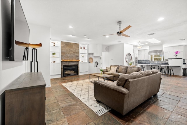 living room featuring stone tile floors, a ceiling fan, recessed lighting, and built in shelves