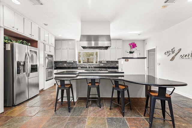 kitchen featuring dark countertops, tasteful backsplash, stone tile floors, stainless steel appliances, and white cabinets