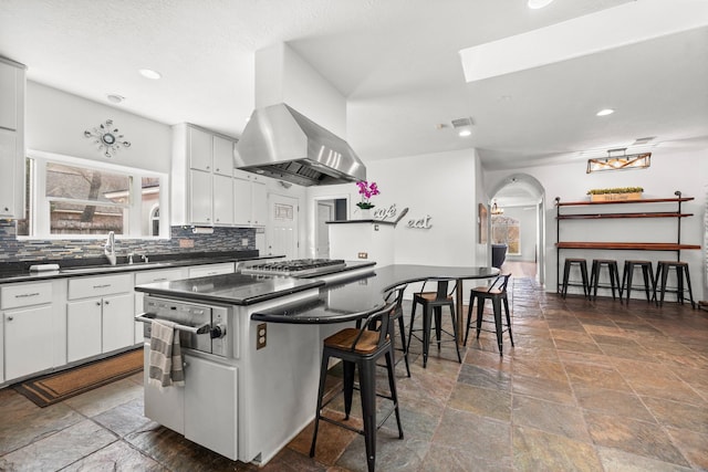 kitchen with stainless steel gas cooktop, dark countertops, stone tile floors, and a kitchen bar