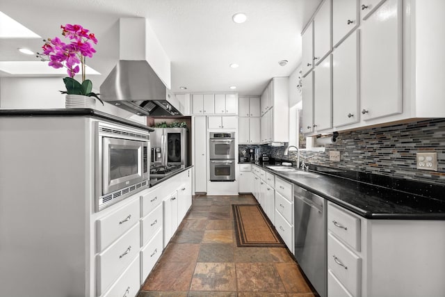 kitchen with island exhaust hood, dark countertops, a sink, stone tile flooring, and appliances with stainless steel finishes