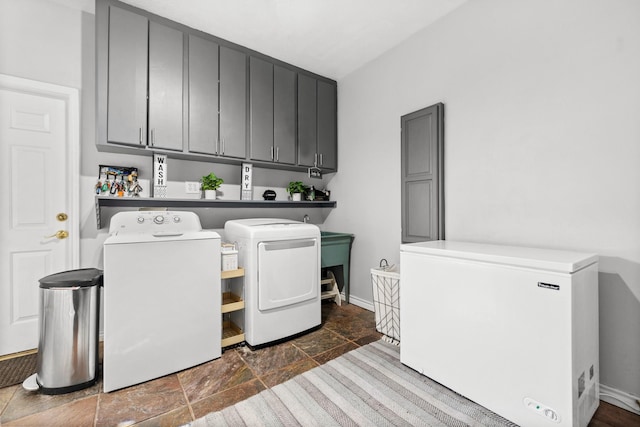 laundry room with cabinet space, stone tile floors, washing machine and clothes dryer, and baseboards