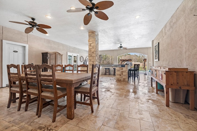 dining space featuring a textured ceiling, stone tile floors, recessed lighting, ornate columns, and a ceiling fan