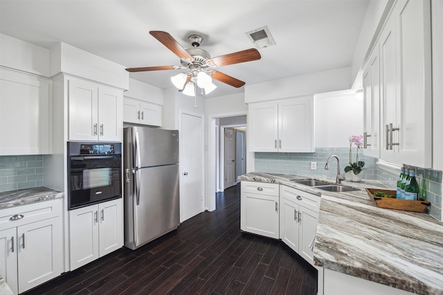 kitchen featuring visible vents, freestanding refrigerator, a sink, oven, and white cabinetry