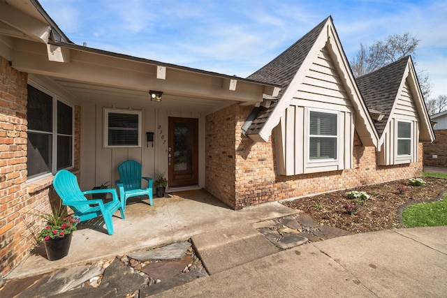 view of exterior entry featuring brick siding, board and batten siding, and roof with shingles