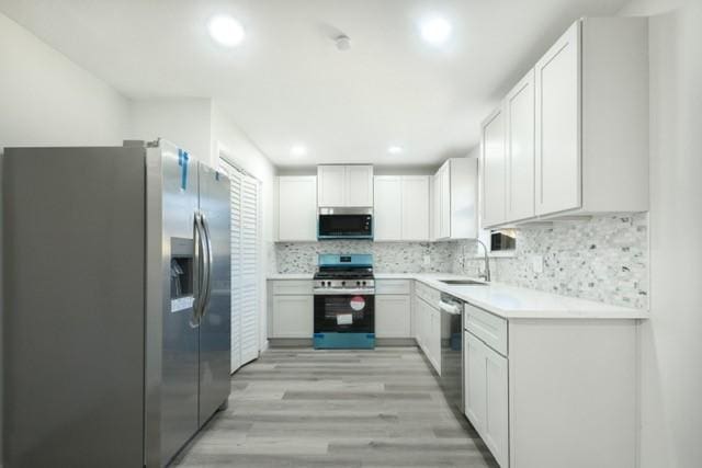 kitchen featuring light wood-style flooring, a sink, light countertops, appliances with stainless steel finishes, and backsplash