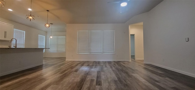 unfurnished living room with dark wood-type flooring, a ceiling fan, baseboards, and vaulted ceiling