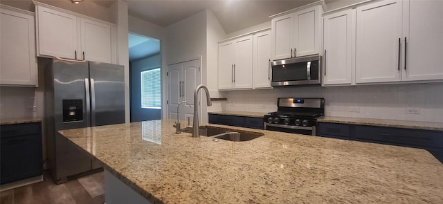 kitchen with a sink, light stone counters, backsplash, white cabinetry, and stainless steel appliances