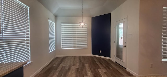 unfurnished dining area featuring dark wood finished floors, a tray ceiling, and baseboards