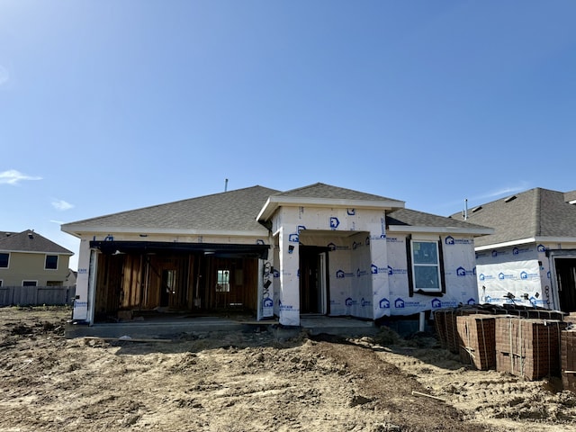 unfinished property with a shingled roof, an attached garage, and fence