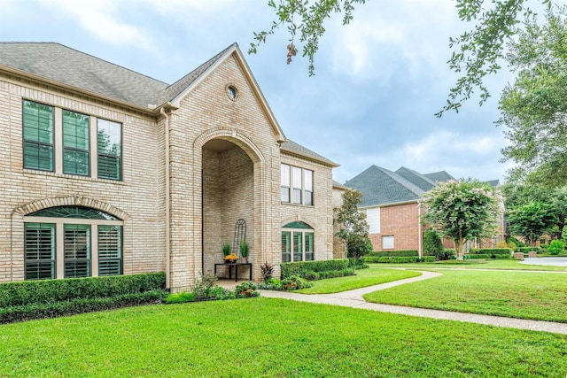 view of front of property featuring brick siding, a front yard, and a shingled roof