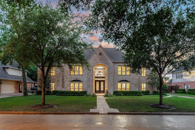 view of front of house with french doors, brick siding, and a yard