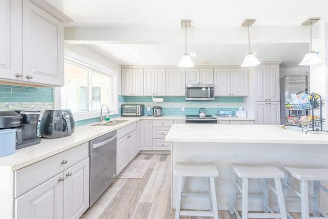 kitchen with light wood finished floors, a sink, decorative backsplash, appliances with stainless steel finishes, and a kitchen bar