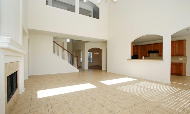 unfurnished living room featuring stairway, light tile patterned floors, baseboards, a fireplace, and arched walkways