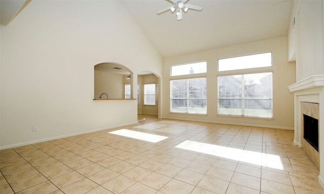 unfurnished living room with baseboards, light tile patterned floors, a fireplace, high vaulted ceiling, and a ceiling fan