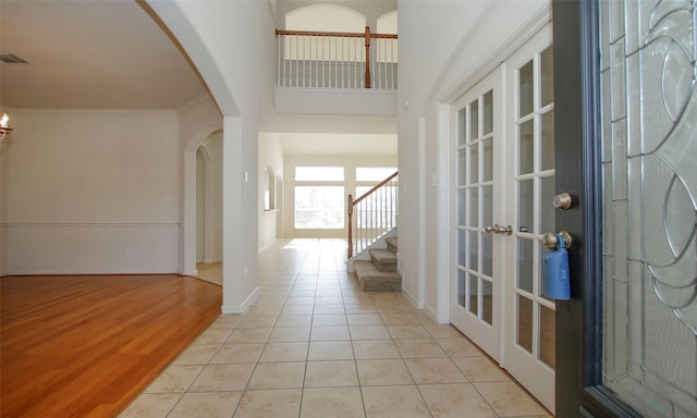 entrance foyer featuring crown molding, baseboards, stairs, arched walkways, and light tile patterned flooring