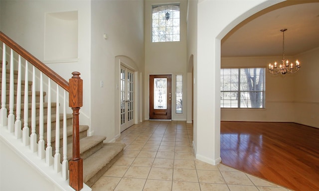 entryway with stairs, ornamental molding, light tile patterned floors, arched walkways, and a notable chandelier