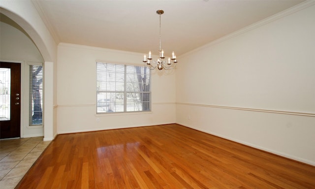 unfurnished room featuring wood finished floors, arched walkways, crown molding, baseboards, and a chandelier