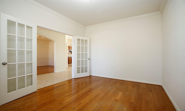 spare room featuring ornamental molding, wood finished floors, french doors, arched walkways, and baseboards