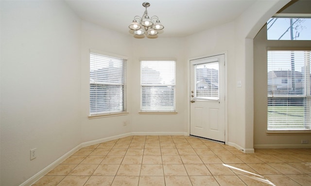 doorway to outside with a notable chandelier, light tile patterned floors, arched walkways, and baseboards