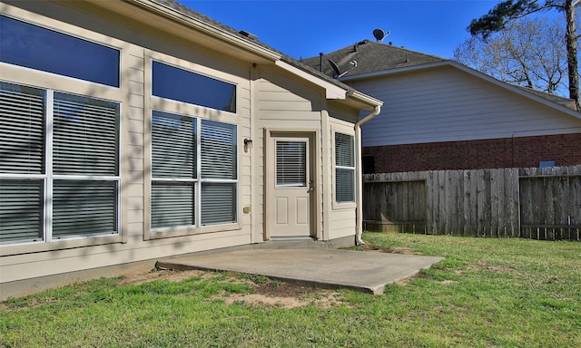 entrance to property with a patio area, a lawn, and fence