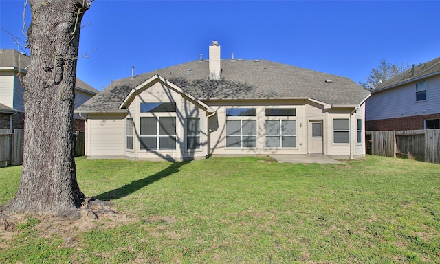 back of house with a patio, a fenced backyard, a yard, a shingled roof, and a chimney