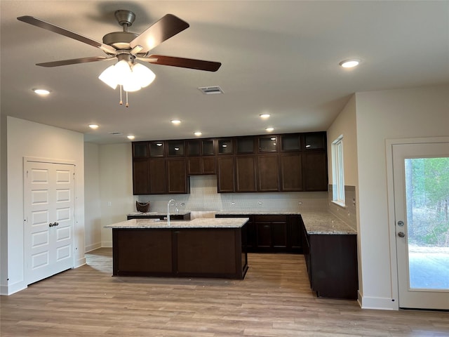 kitchen featuring visible vents, light wood-style flooring, a sink, dark brown cabinetry, and backsplash