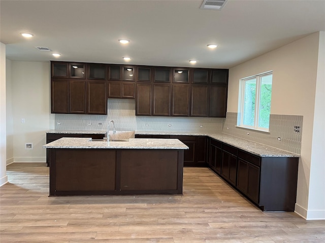 kitchen featuring dark brown cabinetry, light wood finished floors, tasteful backsplash, and a sink