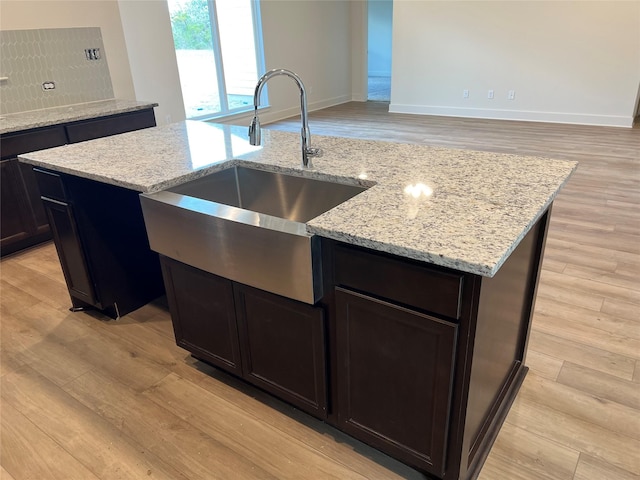 kitchen with light wood finished floors, light stone countertops, a kitchen island with sink, and a sink