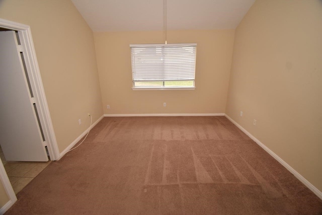 carpeted empty room with tile patterned flooring, baseboards, and lofted ceiling