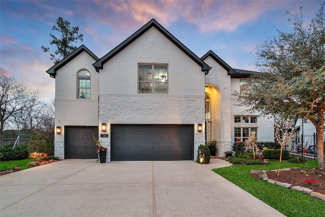 french country inspired facade with a garage, stone siding, brick siding, and concrete driveway