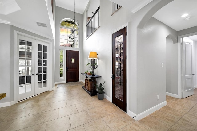 foyer featuring tile patterned floors, french doors, arched walkways, baseboards, and a towering ceiling