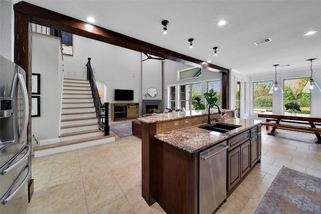 kitchen featuring light stone countertops, visible vents, a warm lit fireplace, a sink, and stainless steel appliances