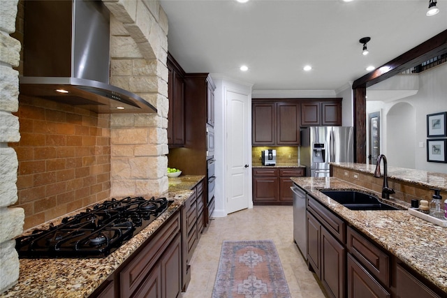 kitchen featuring arched walkways, a sink, appliances with stainless steel finishes, wall chimney range hood, and tasteful backsplash