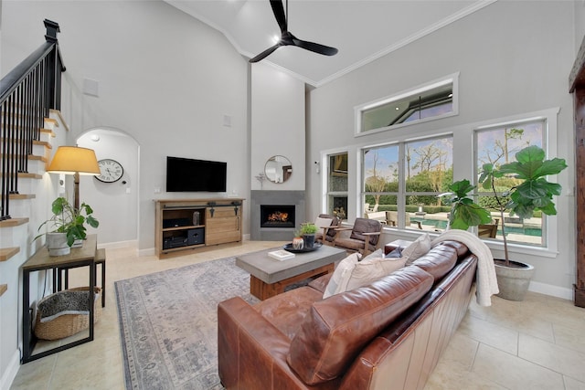 living room with stairway, a lit fireplace, crown molding, baseboards, and ceiling fan