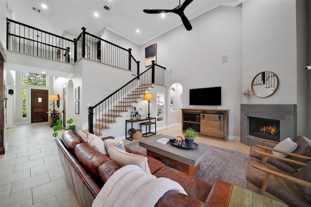 living room featuring stairway, a lit fireplace, light tile patterned floors, arched walkways, and a ceiling fan