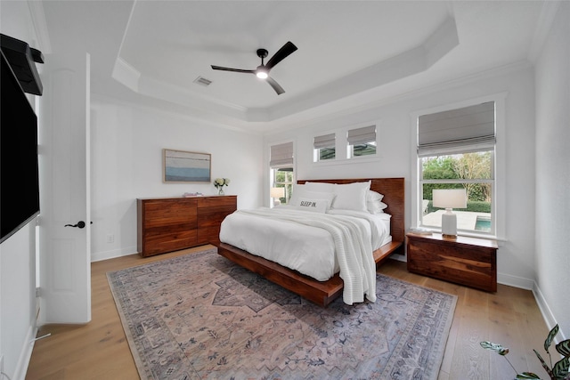 bedroom with light wood-type flooring, visible vents, a raised ceiling, and baseboards