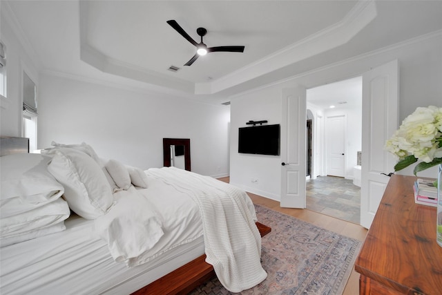 bedroom featuring visible vents, light wood-style flooring, crown molding, and a raised ceiling