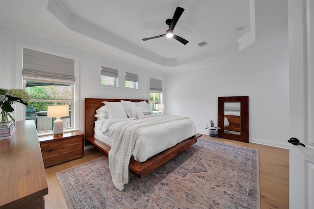 bedroom featuring a tray ceiling, multiple windows, and ornamental molding