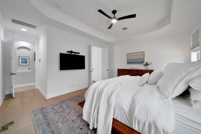 bedroom featuring a tray ceiling, visible vents, ornamental molding, and light wood finished floors