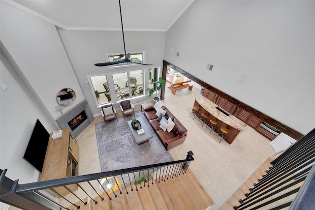 living room with visible vents, baseboards, a fireplace, a towering ceiling, and crown molding