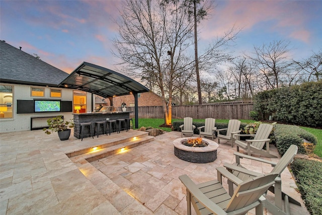 patio terrace at dusk with fence private yard, outdoor dry bar, and an outdoor fire pit