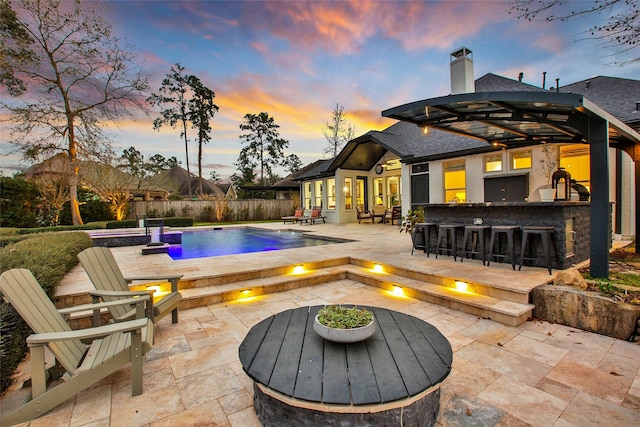 view of swimming pool with outdoor dry bar, a patio, fence, a fire pit, and a fenced in pool