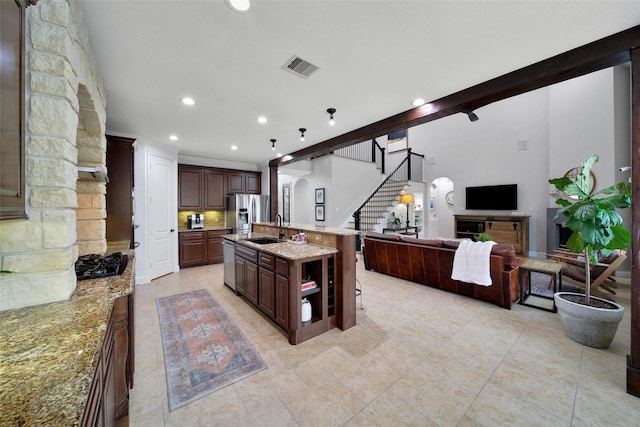 kitchen with light stone counters, visible vents, a kitchen island with sink, stainless steel fridge, and open floor plan