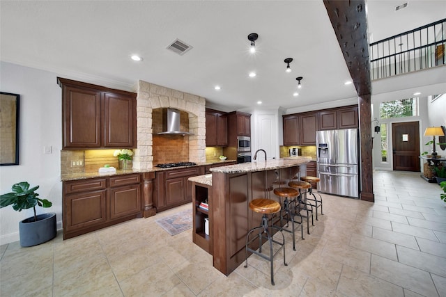 kitchen with visible vents, a kitchen breakfast bar, appliances with stainless steel finishes, wall chimney exhaust hood, and decorative backsplash