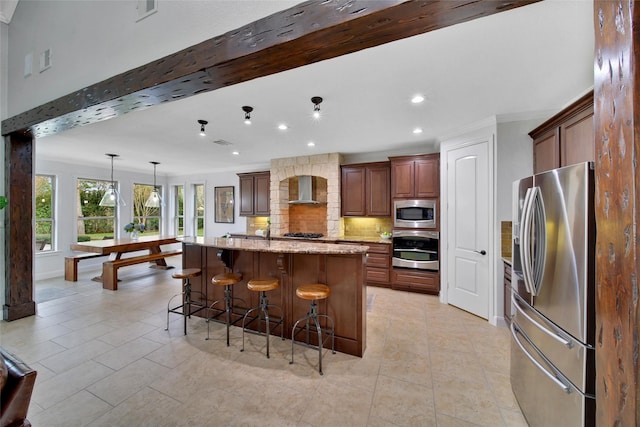 kitchen with backsplash, light stone countertops, a kitchen breakfast bar, stainless steel appliances, and wall chimney exhaust hood