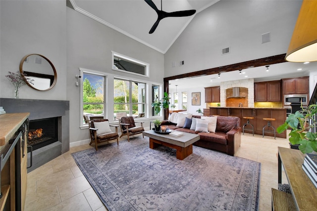 living area with baseboards, high vaulted ceiling, ceiling fan, ornamental molding, and a lit fireplace