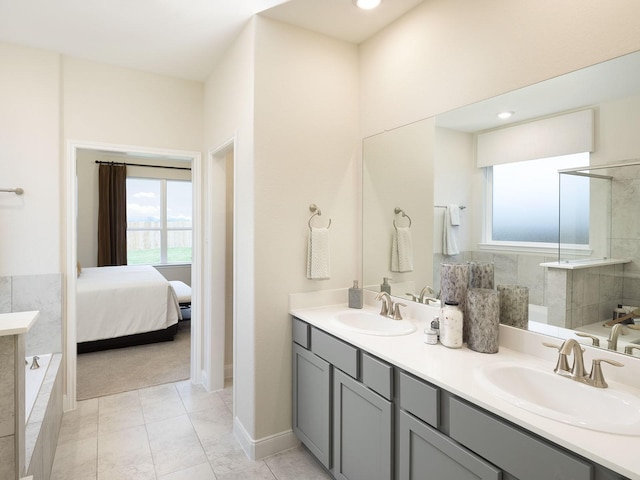 ensuite bathroom with double vanity, tile patterned floors, tiled bath, and a sink