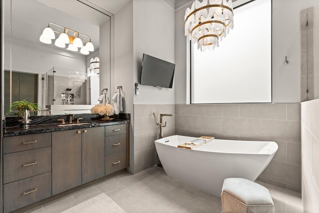 full bath with tile patterned floors, tile walls, wainscoting, a soaking tub, and vanity